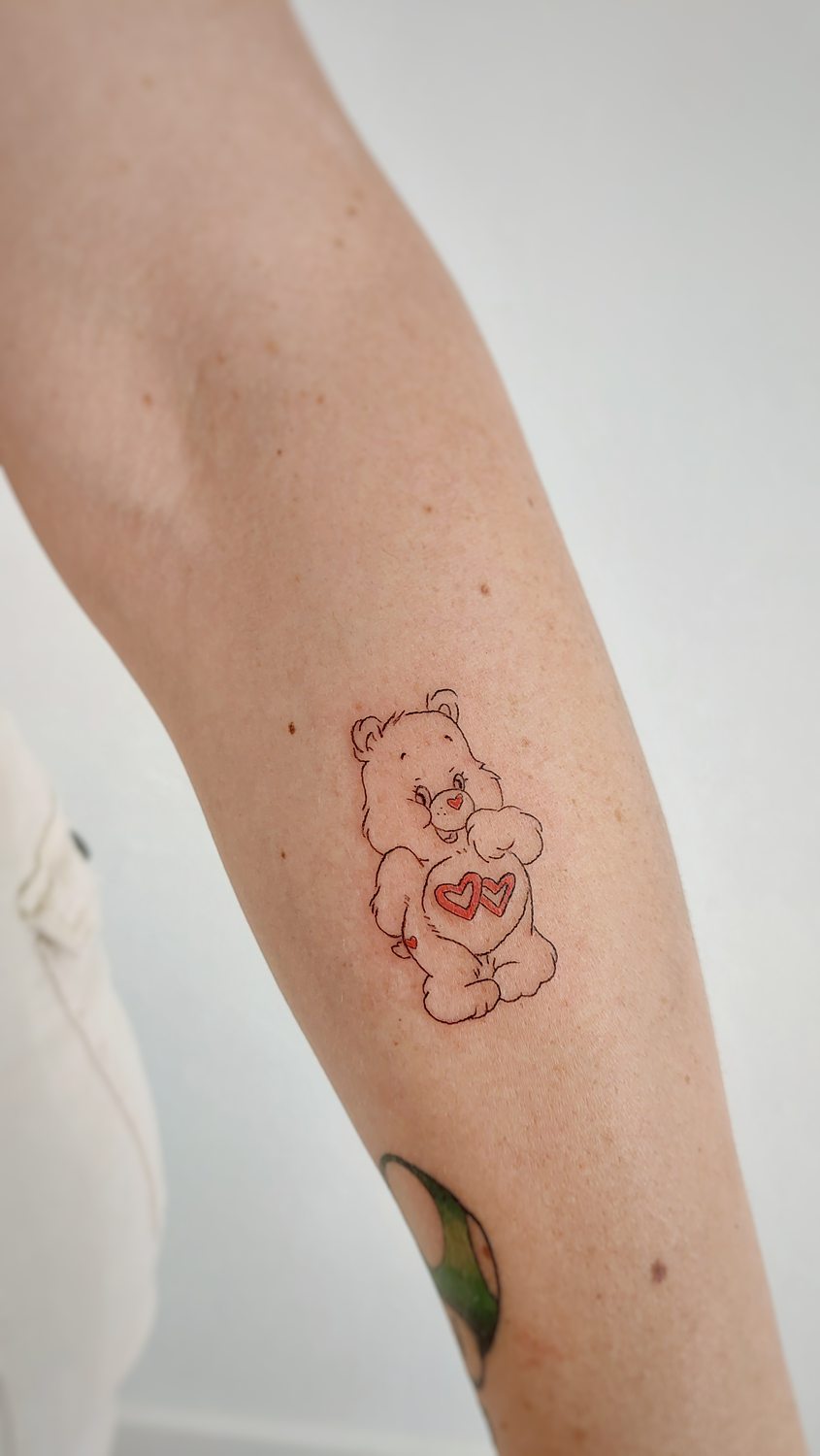 Tatuaje de oso amoroso (care bear) en el brazo hecho con técnica de línea fina en un estudio de Valencia