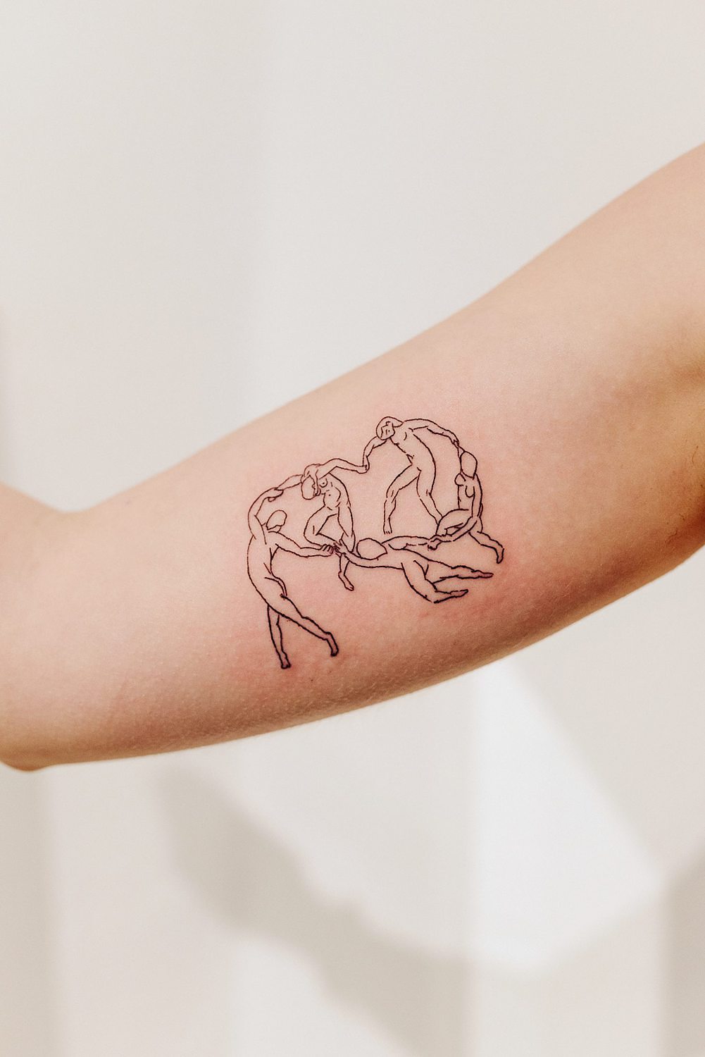 Tatuaje minimalista de figuras humanas en el brazo.