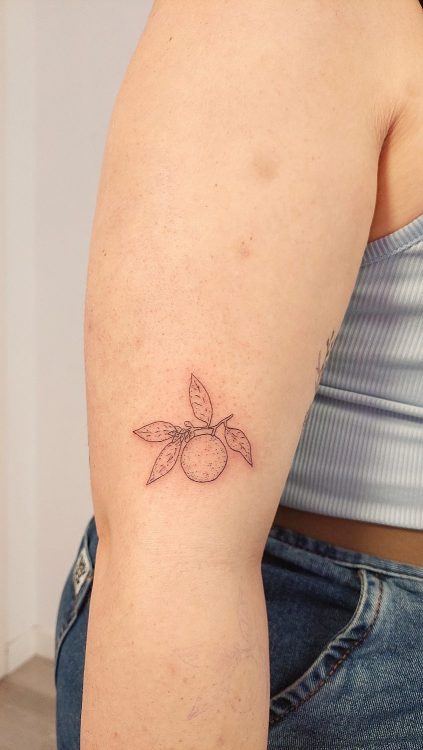 Tatuaje de naranja con hojas en brazo hecho con técnica de línea fina en un estudio de Valencia