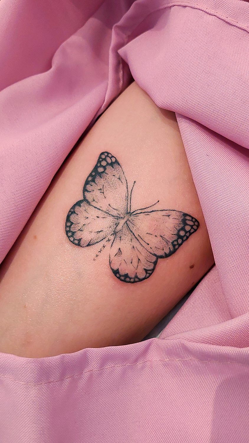 Tatuaje de mariposa en el brazo con tela rosa de fondo
