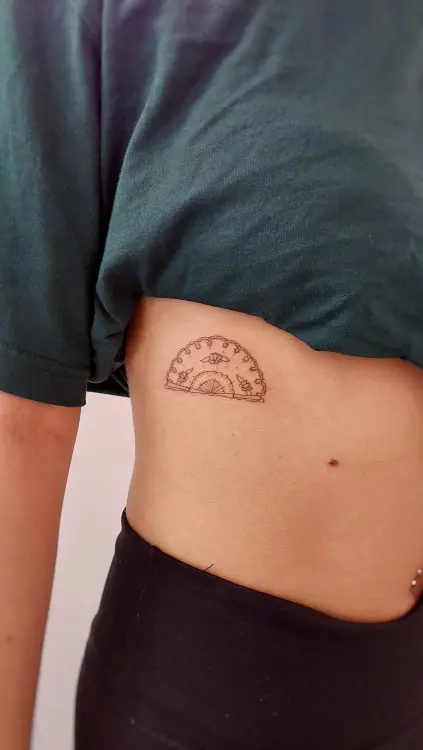 Tatuaje pequeño de abanico en el costado hecho con técnica de línea fina en un estudio de Valencia