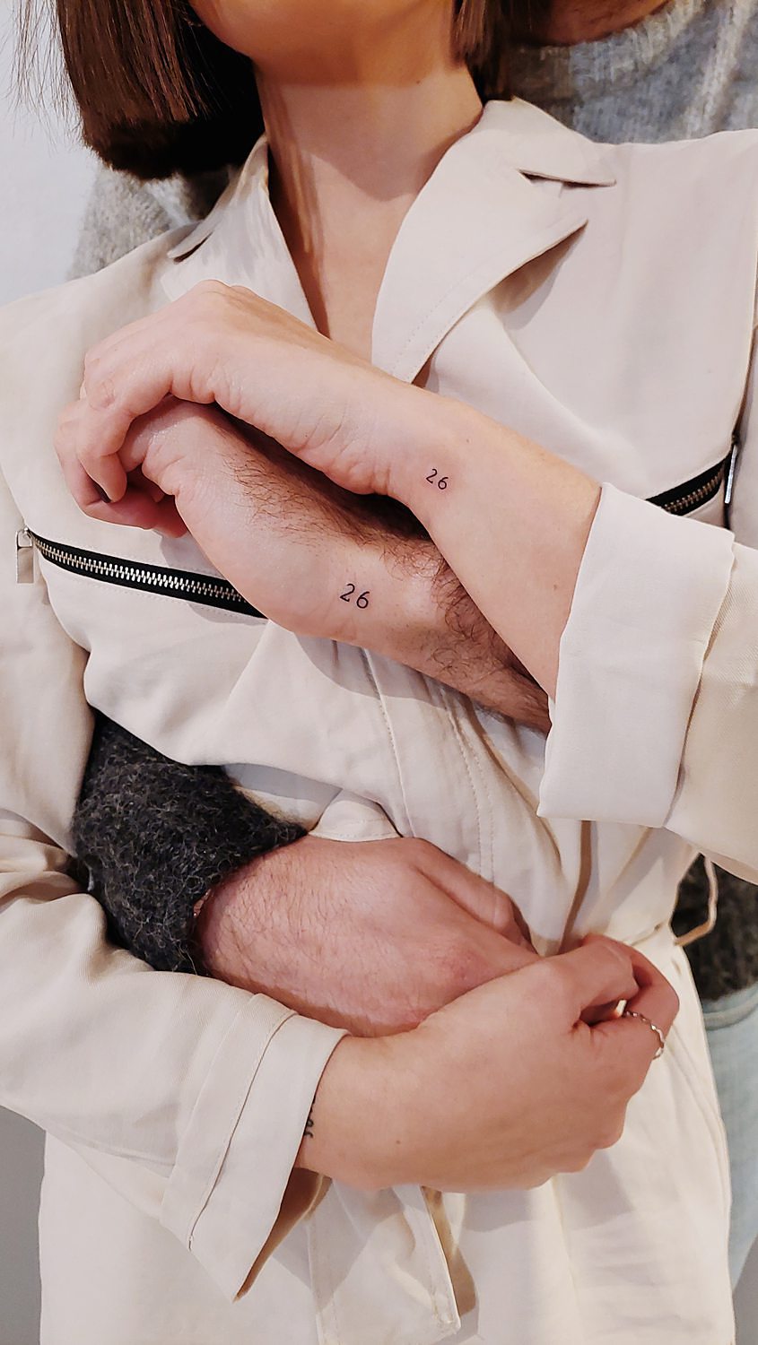 Couple with matching number 26 wrist tattoos.