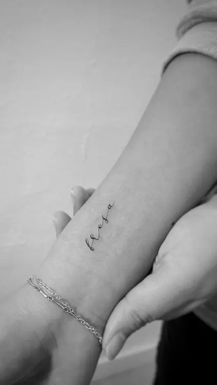 Brazo con tatuaje de palabra en cursiva en la que se lee "Fresa" hecho usando técnicas de tatuado de línea fina