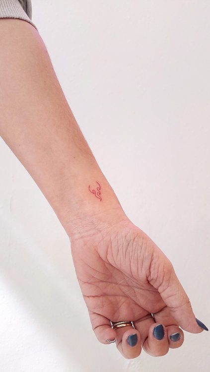 Tatuaje llama de fuego con tinta roja minimalista en la muñeca de mujer