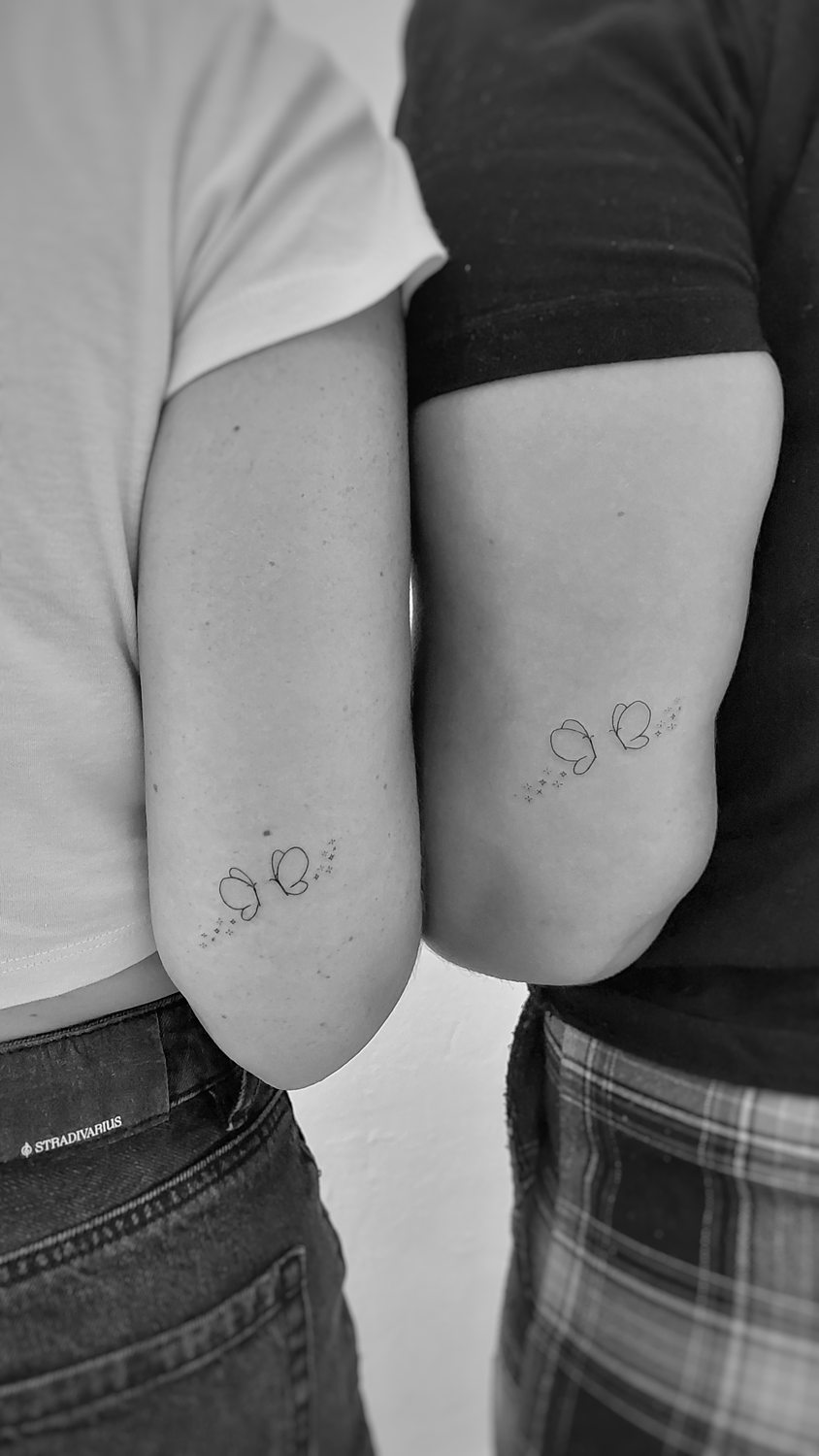 Tatuaje minimalista de mariposa en brazos de pareja.