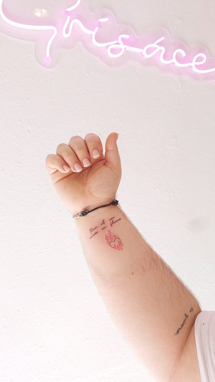 Brazo con tatuaje de texto "Tinc el cor encés en flama" y llama roja.