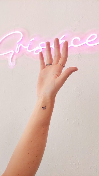 Mini butterfly tattoo near a woman's wrist, neon sign background