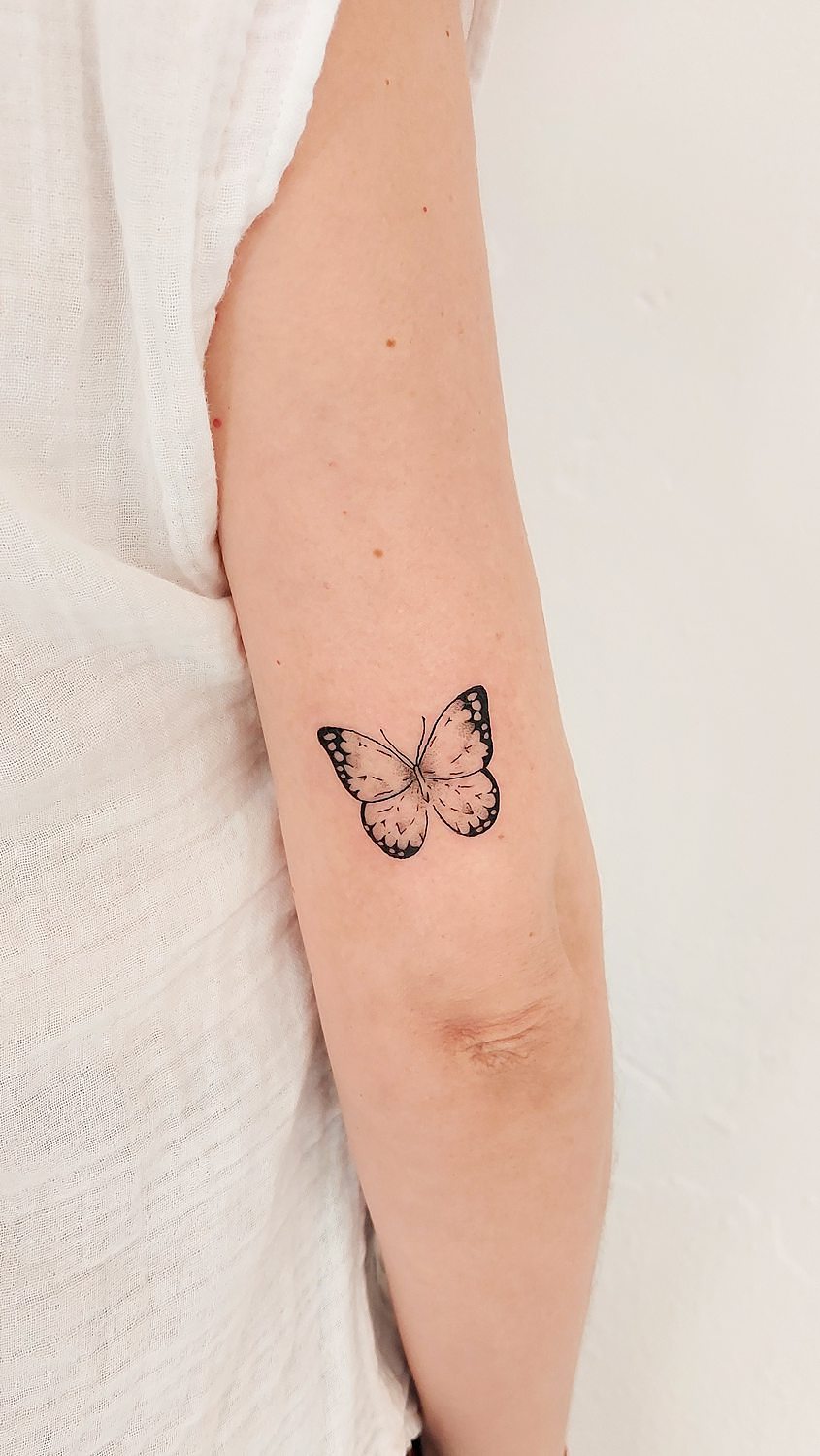 Tatuaje de mariposa minimalista en brazo de mujer.