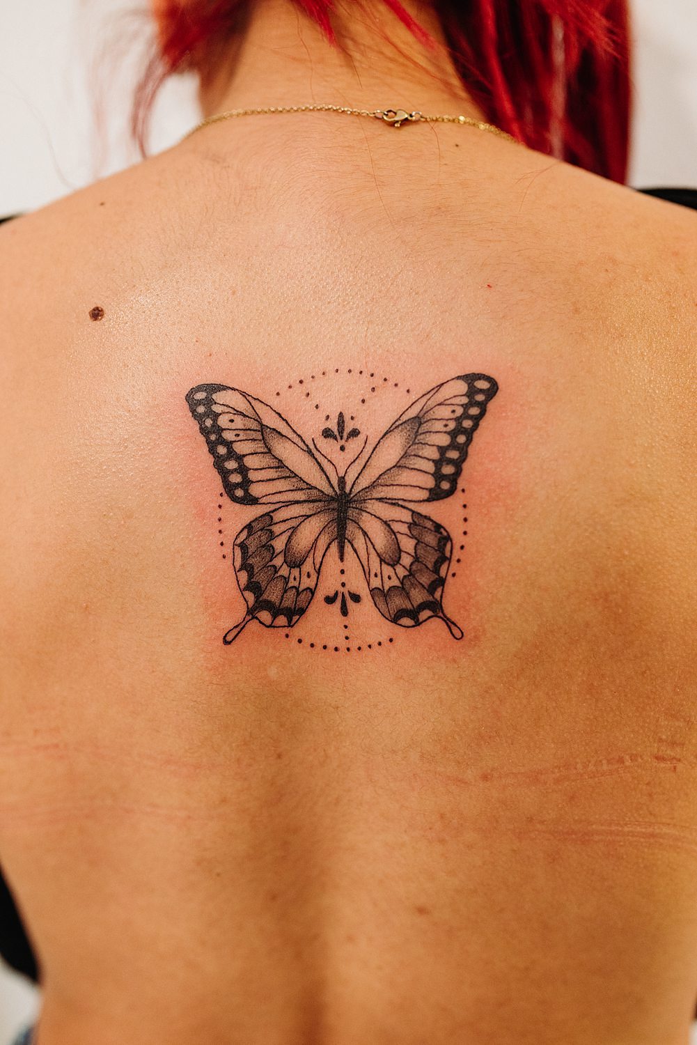 Tatuaje mariposa en la espalda de mujer pelirroja.