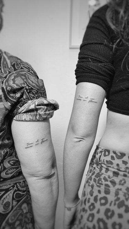 Dos brazos tatuados con texto en cursiva.