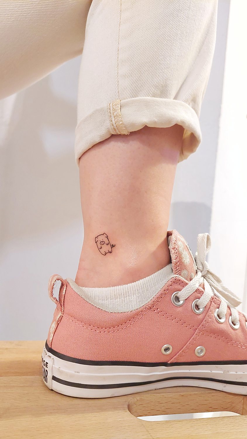 Tatuaje de cerdito en tobillo con zapatilla rosa.