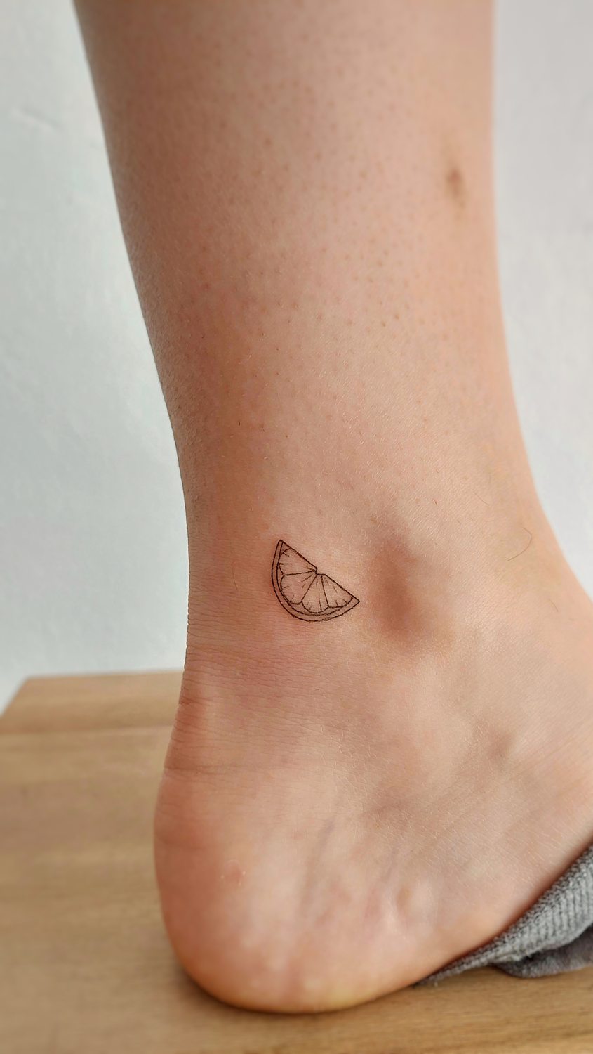 Tatuaje de rodaja de limón en tobillo.