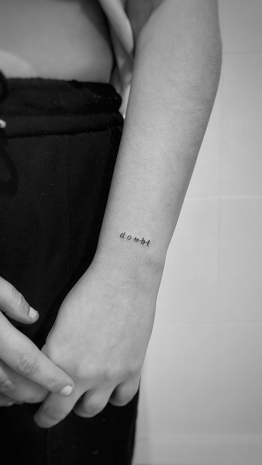 Tatuaje de la palabra "Doubt" con la parte de "ubt" tachada en la muñeca de una mujer