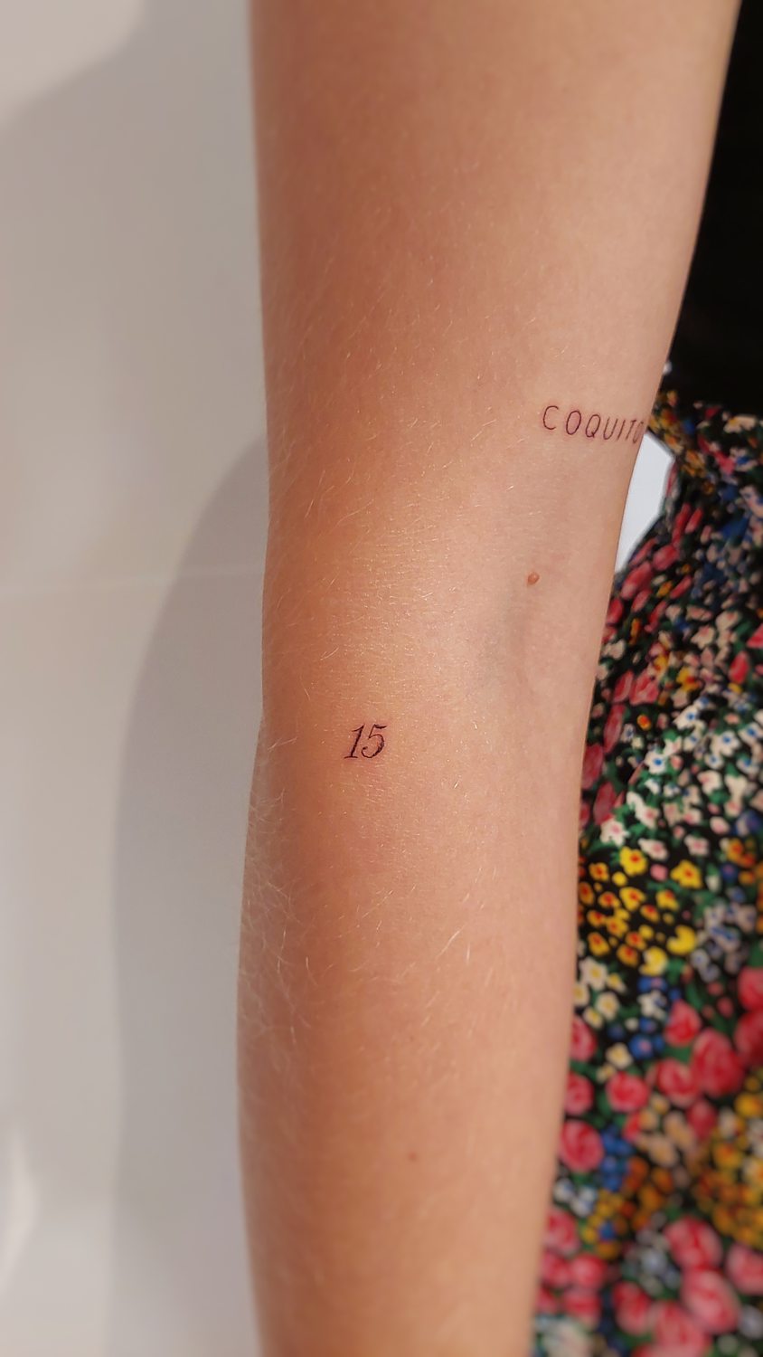 Tatuaje del número 15 en brazo de mujer con vestido de flores colorido