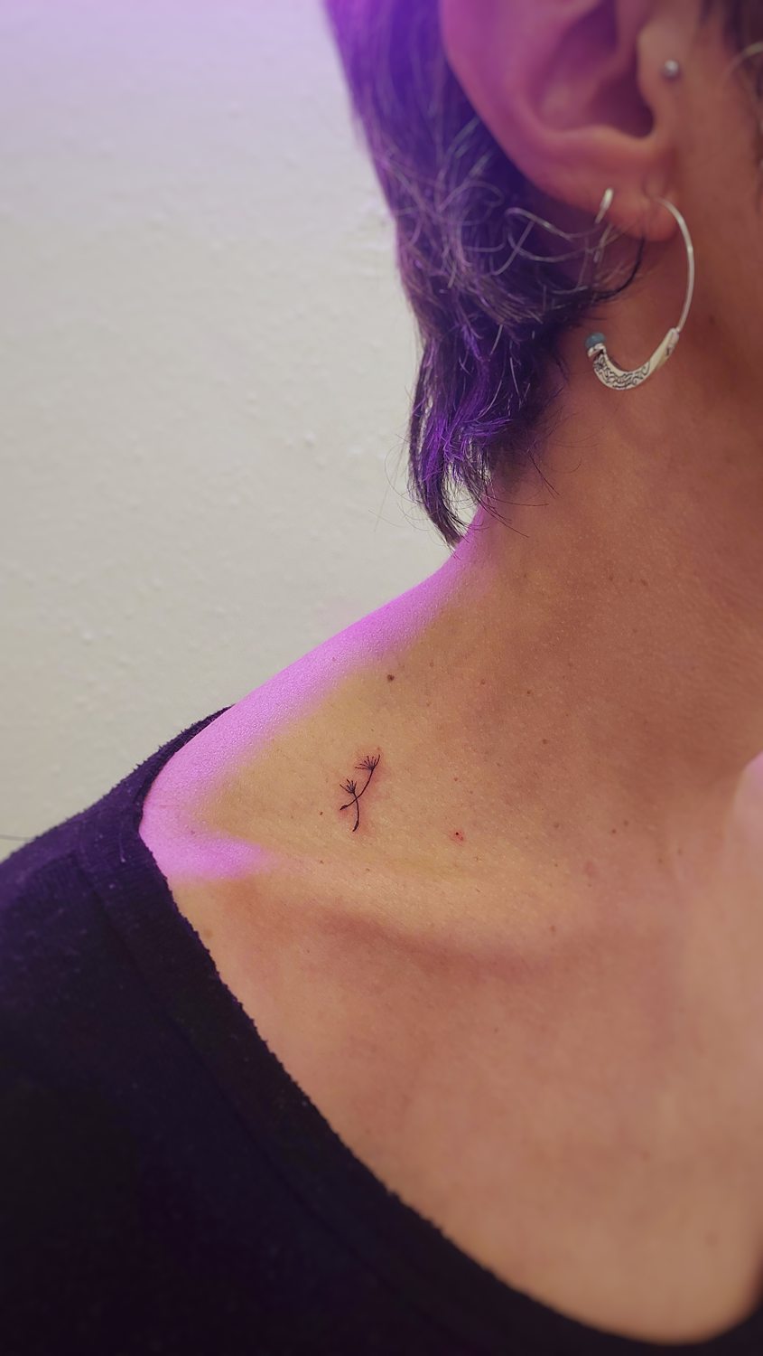 Tatuaje delicado de dientes de león en el cuello de una mujer.