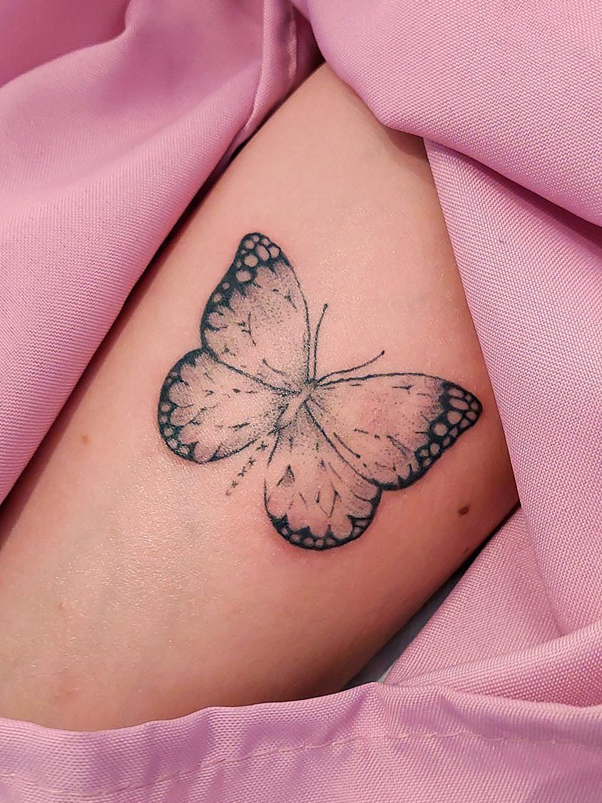 Tatuaje de mariposa en tinta negra sobre piel clara.