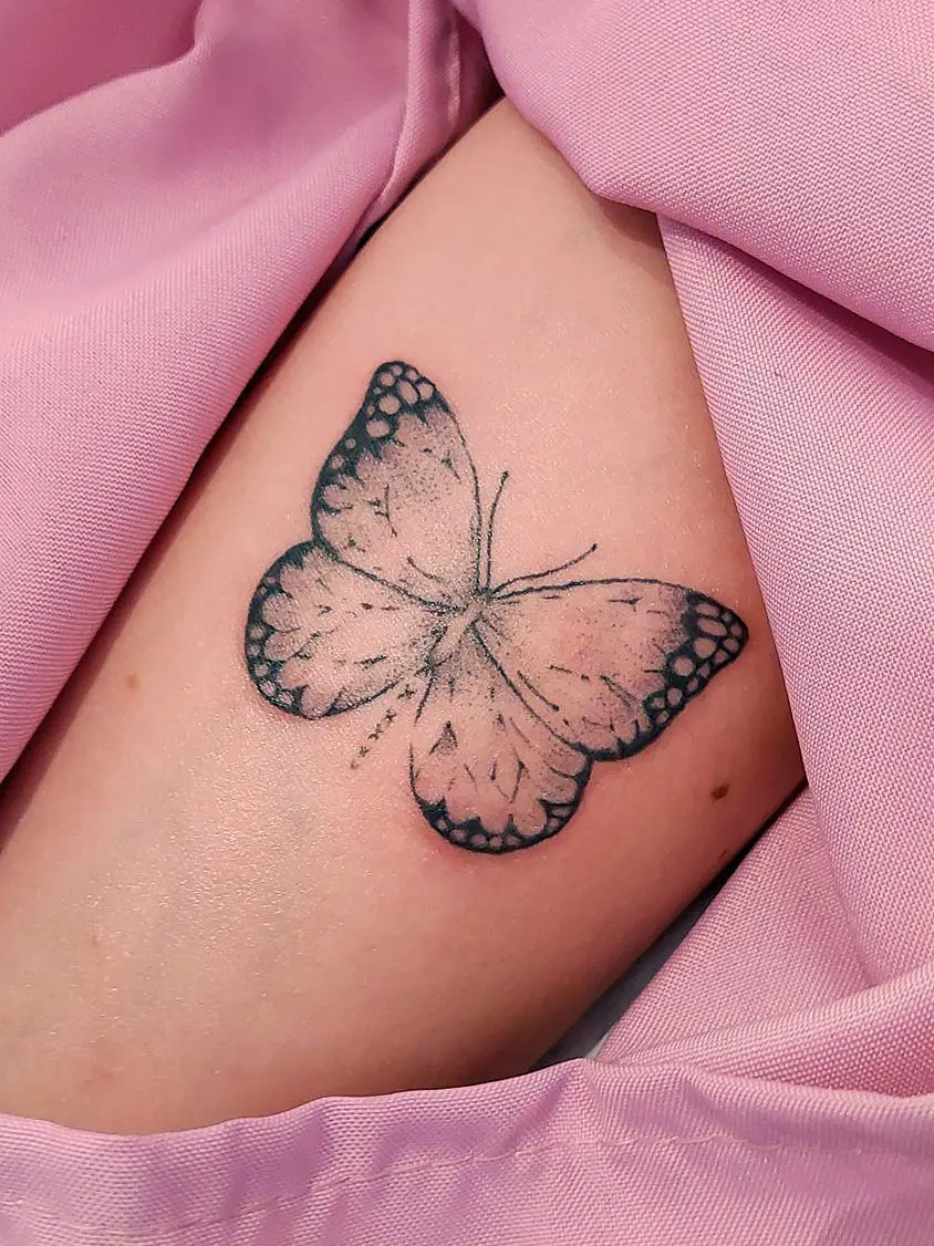 Tatuaje de mariposa en tinta negra sobre piel clara.
