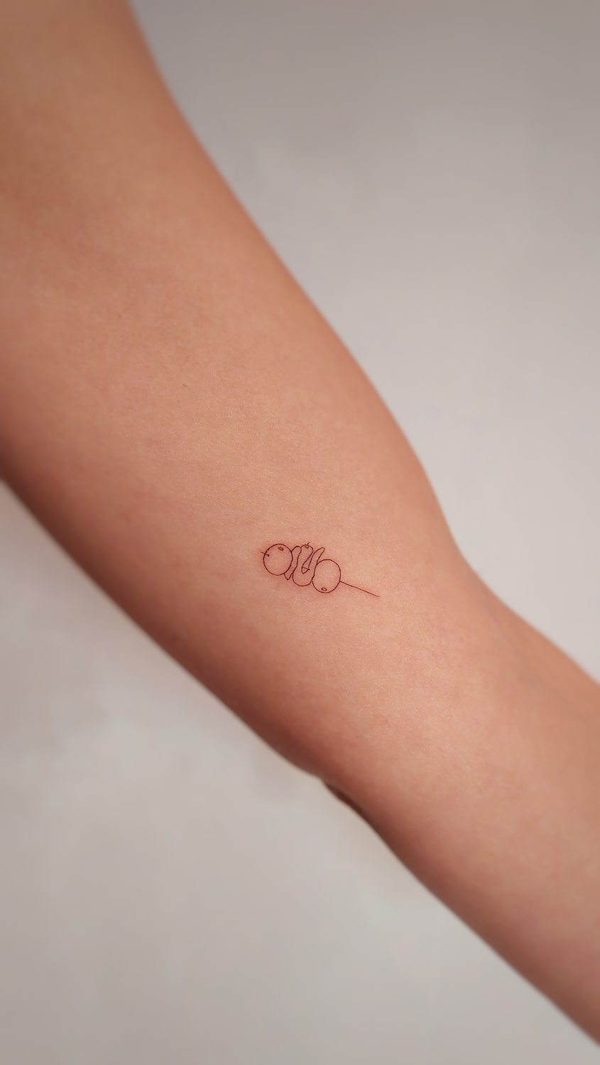 Tatuaje minimalista de dango en un palillo en la piel.