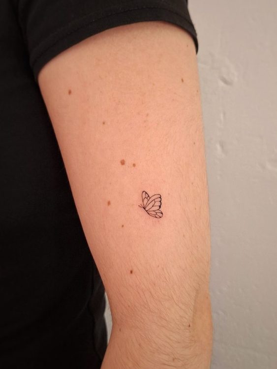 Tatuaje minimalista de mariposa en el brazo de una persona.