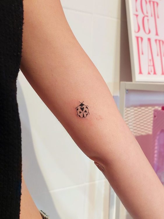 Tatuaje minimalista de mariquita con corazones en el brazo