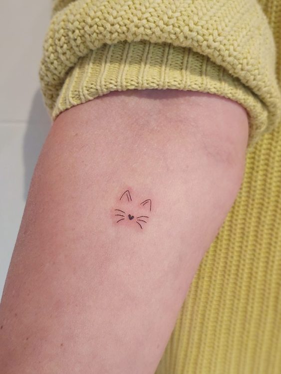 Tatuaje de cara de gato minimalista en brazo.