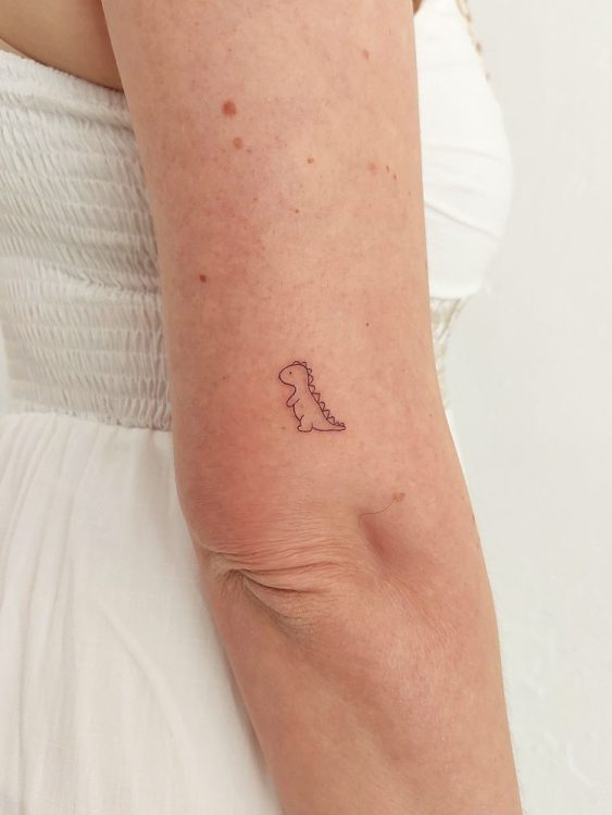 Tatuaje minimalista de dinosaurio en el brazo de una persona.