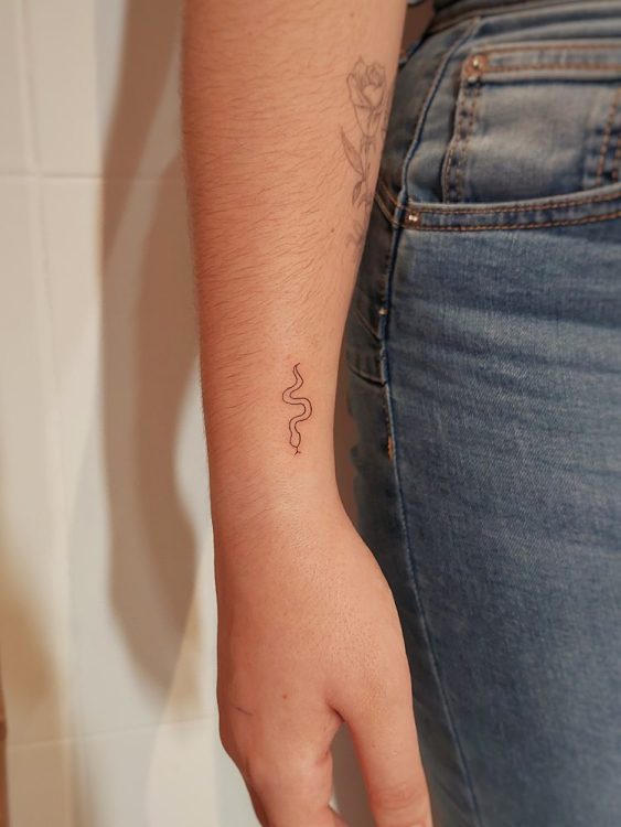 Tatuaje de serpiente fina en la muñeca de una persona.