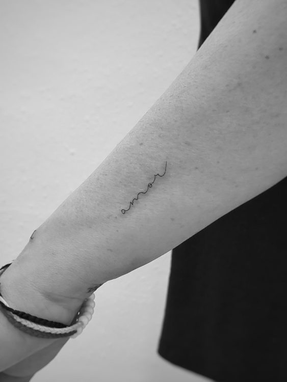 Tatuaje de la palabra "amor" escrita a mano en el antebrazo.